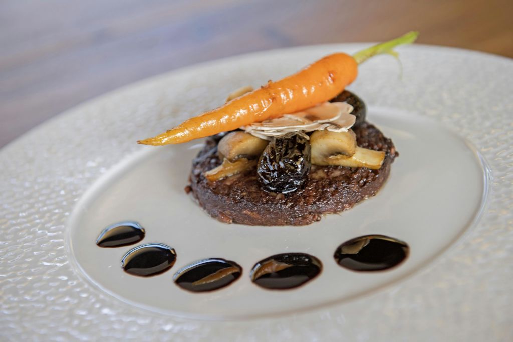 도금된 미식가 요리는 버섯이 들어간 패티 위에 구운 당근과 슬라이스 아몬드, 발사믹 도트가 장식되어 있습니다.