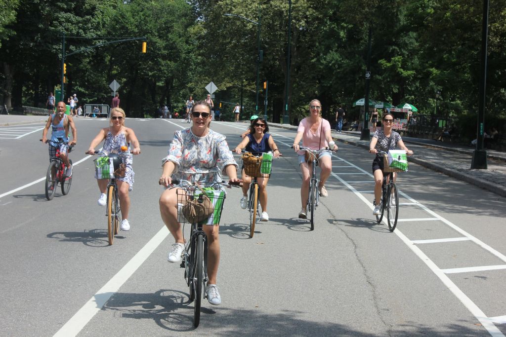 나무가 우거진 거리에서 자전거를 타고 웃으며 화창한 하루를 즐기는 5명의 사람들.