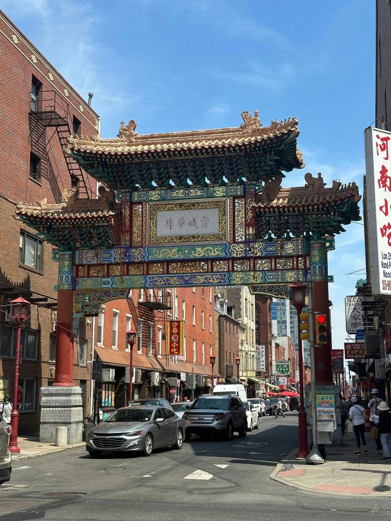 화창한 날 자동차, 보행자, 건물이 즐비한 번화한 도시 거리에 화려한 중국식 대문이 서 있습니다.