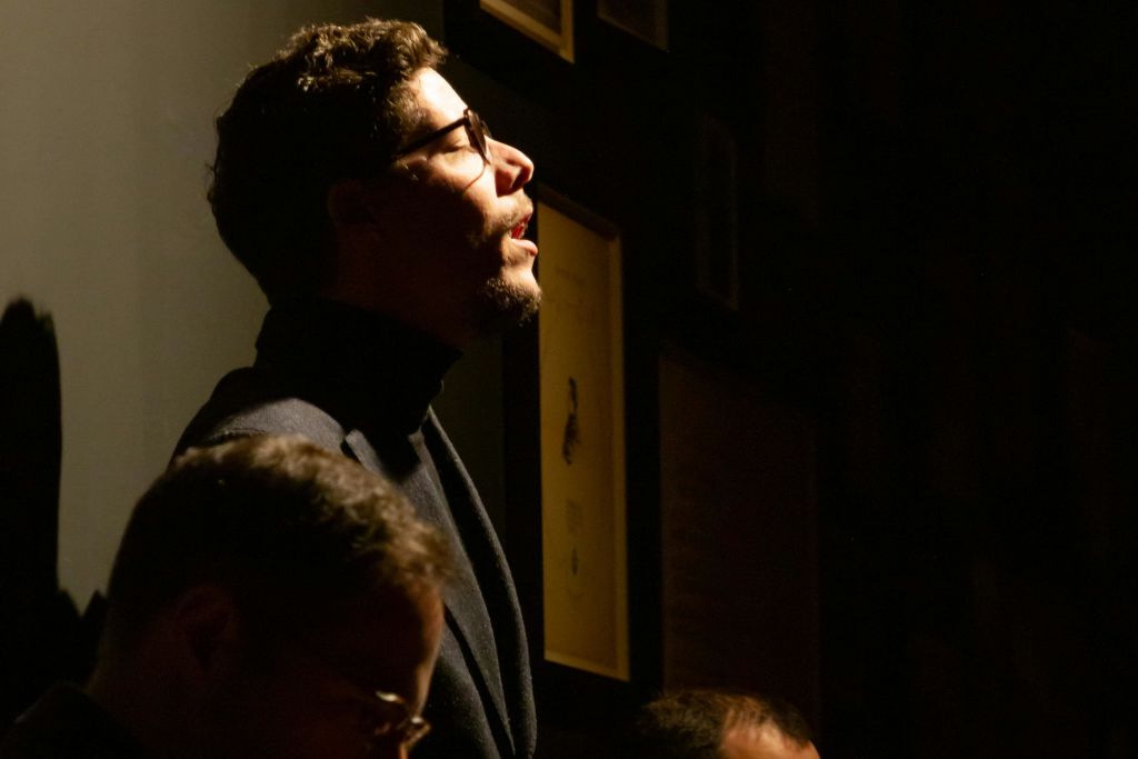 안경과 수염을 가진 남성이 어두운 터틀넥을 착용하고 액자에 담긴 사진으로 어두운 배경을 배경으로 극적인 조명을 받고 있습니다.