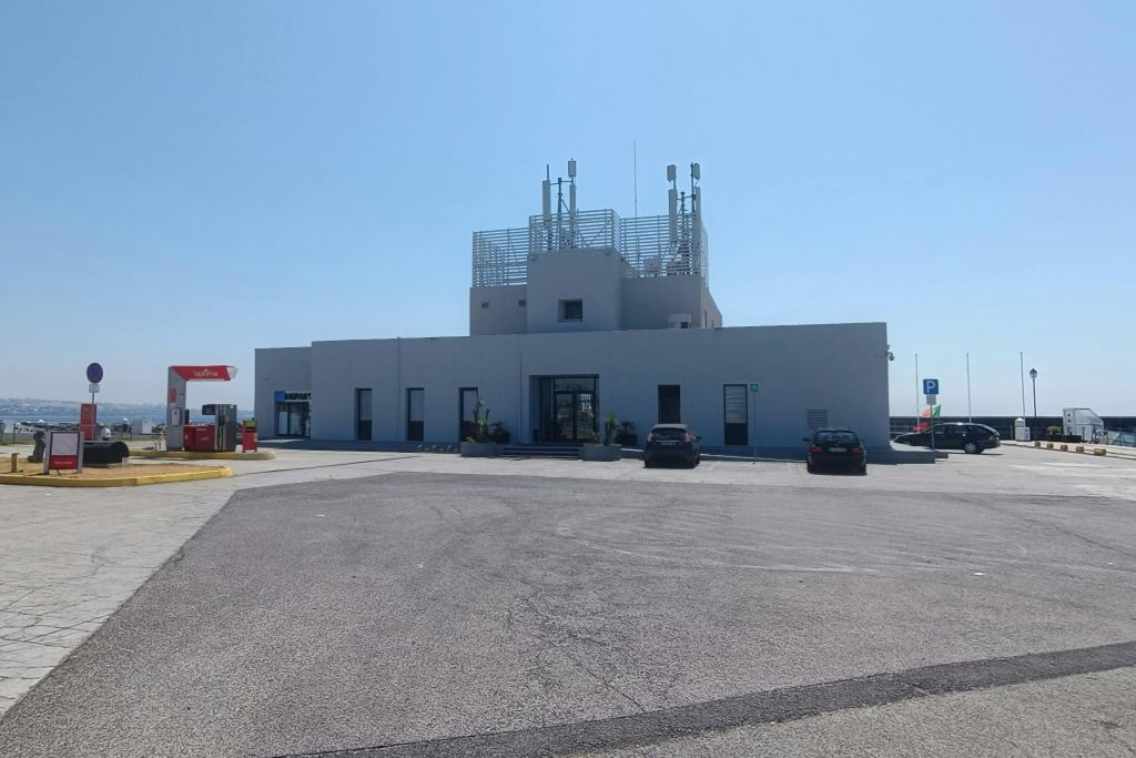 지붕에 안테나, 포장된 주차 공간, 화창한 날 앞에 주차된 차량 2대가 있는 현대적인 단층 흰색 건물입니다.