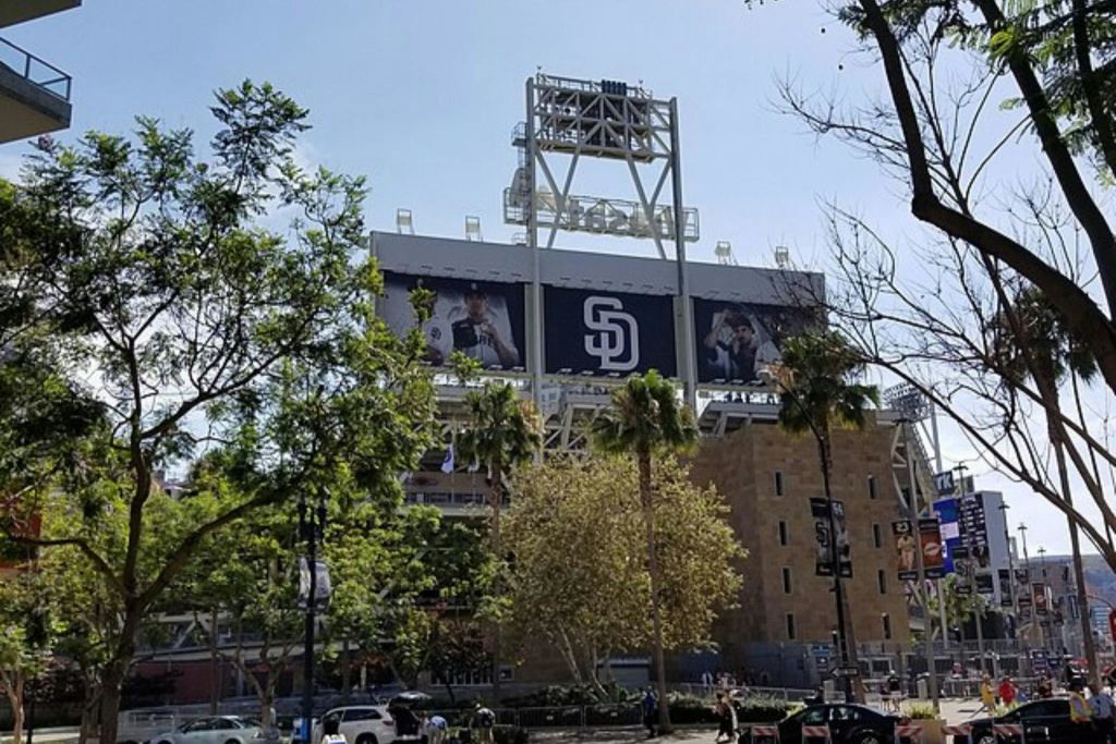 커다란 샌디에이고 파드레스 로고와 선수 배너가 있는 경기장 외관은 나무와 맑고 푸른 하늘로 둘러싸여 있습니다.