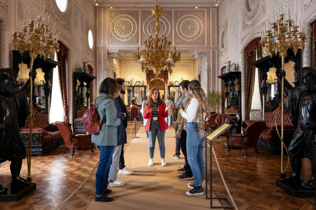 샹들리에, 디테일한 벽, 앤티크한 가구로 꾸며진 화려한 객실에서 투어 가이드가 일행을 이끕니다.