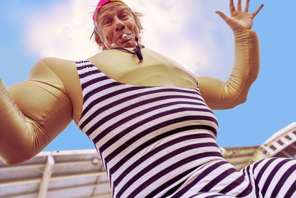 줄무늬 의상과 부풀어 오른 팔 의상을 입고 휘파람을 불며 밝은 하늘을 배경으로 한 사람.