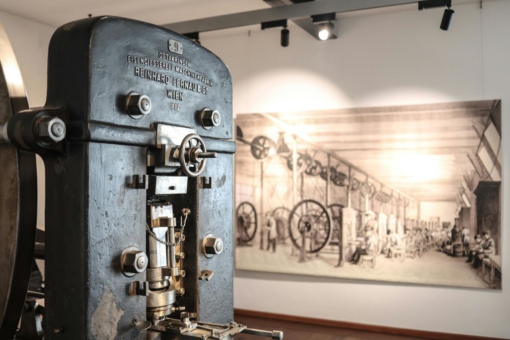 박물관에 전시된 빈티지 산업용 기계로, 기계를 배경으로 한 역사적인 일러스트레이션이 전시되어 있습니다.