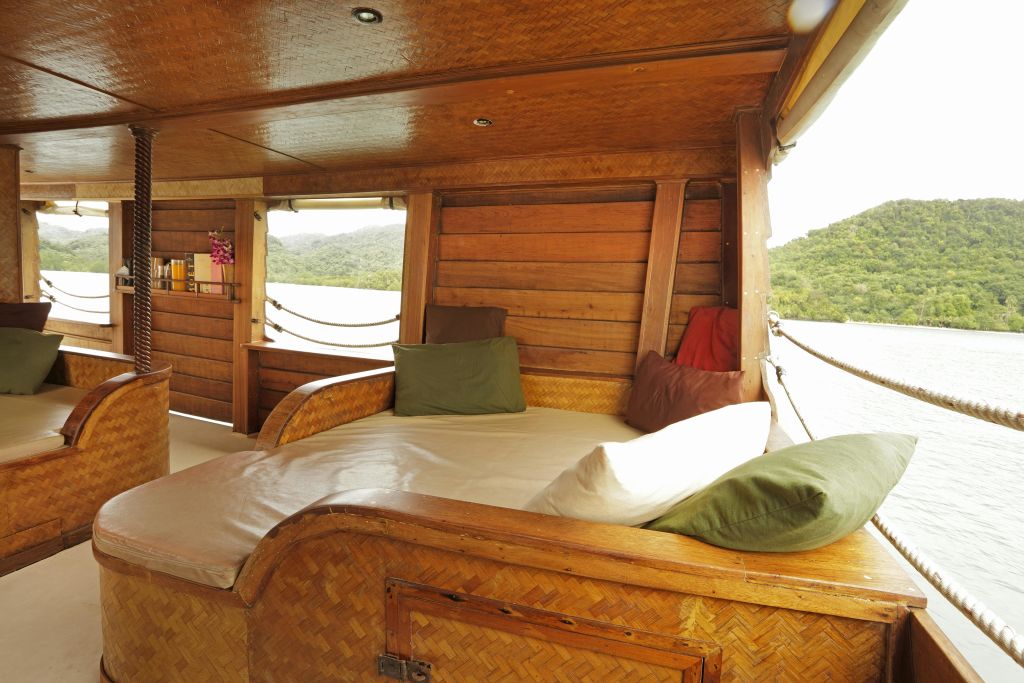 쿠션 벤치, 베개, 물과 숲이 우거진 산의 부분적인 전망이 있는 아늑한 나무 보트 인테리어.