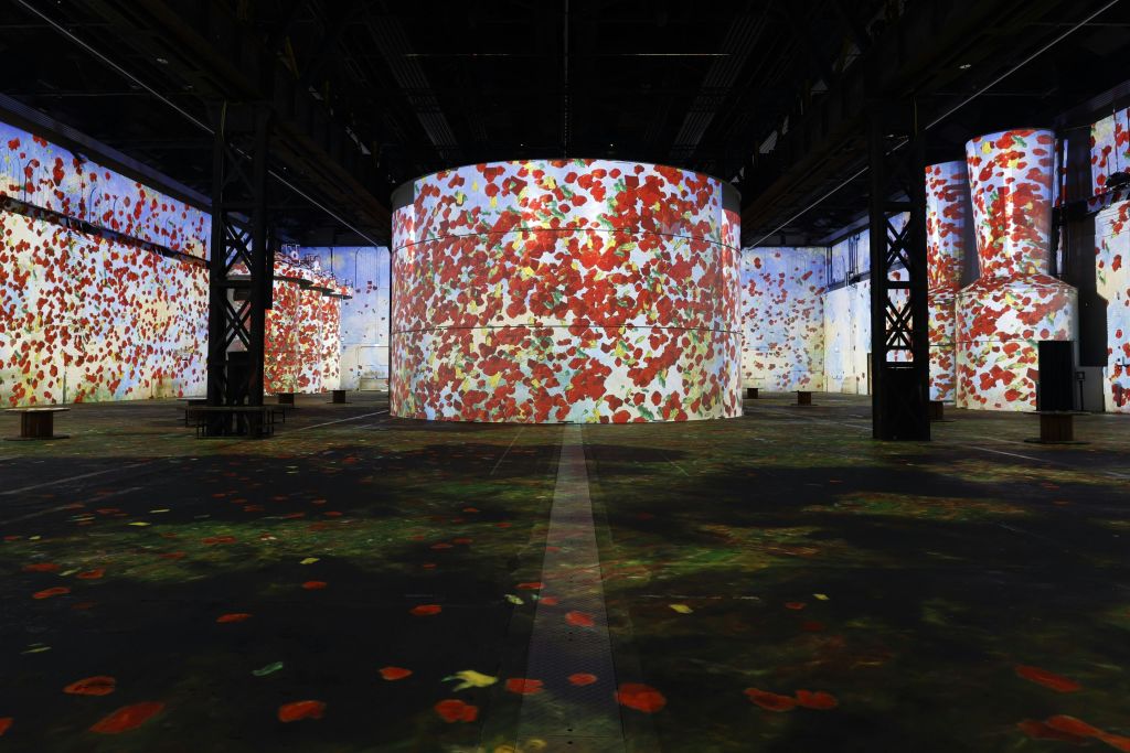 원통형 벽과 플로럴 프로젝션으로 덮인 바닥이 있는 넓은 실내 공간으로, 주로 빨간색과 녹색입니다.