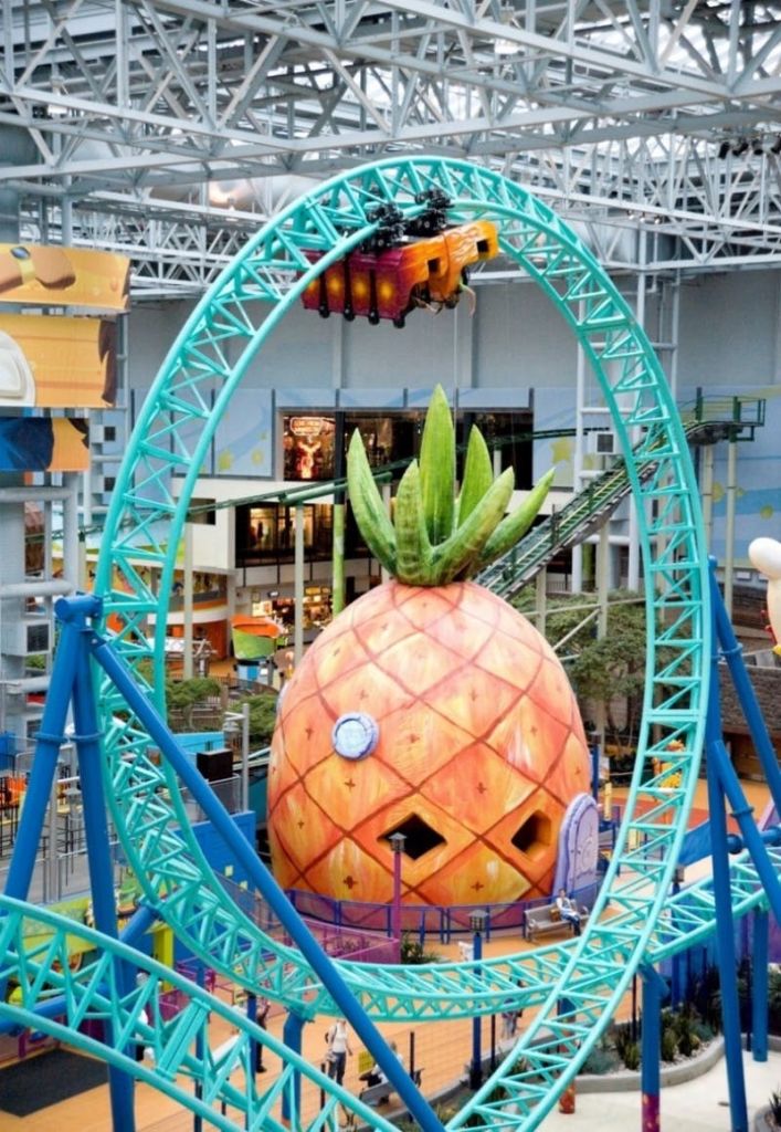 청록색 롤러코스터 루프가 있는 실내 놀이공원 내부에 초록색 잎이 있는 거대한 파인애플 하우스입니다.