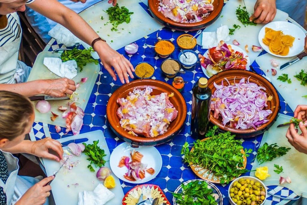 파란색 타일 테이블에 다진 허브, 향신료, 썬 양파로 음식을 준비하는 사람들이 여럿 있습니다.