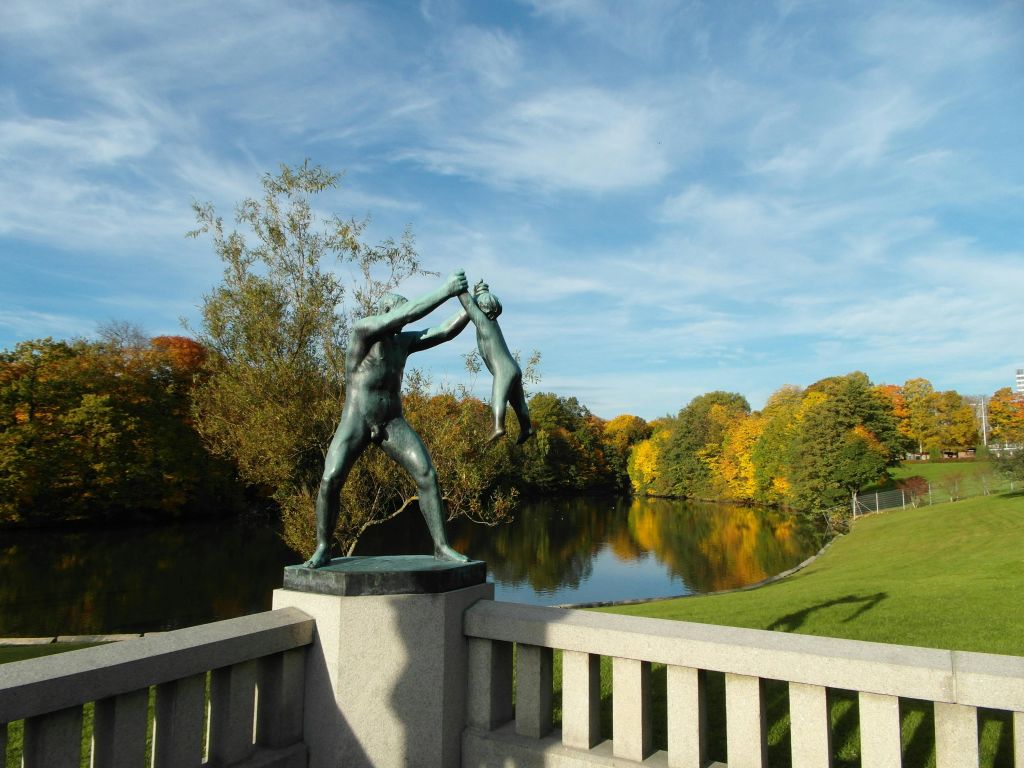 강과 형형색색의 가을 나무가 한눈에 내려다보이는 다리 위에 아이를 안고 있는 한 남자의 동상.