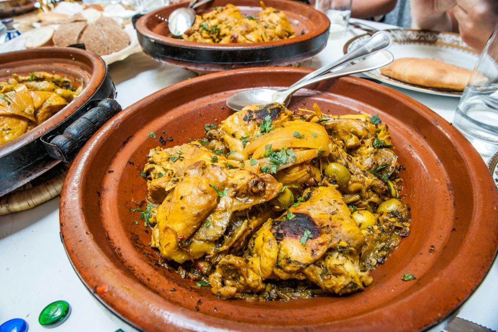 허브와 향신료가 들어간 모로코식 치킨 타긴 요리를 숟가락이 담긴 점토 냄비에 담아 추가 타긴 냄비와 함께 테이블에 놓습니다.