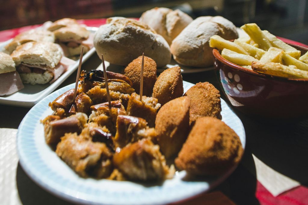 빵 롤과 튀김 그릇으로 둘러싸인 크로켓과 꼬치 튀김 음식이 담긴 접시.