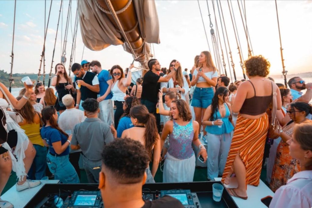 한 무리의 사람들이 보트 갑판에서 돛을 달고 춤을 추며 사교를 즐기고 있습니다.