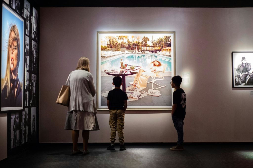 나이든 여성과 두 명의 어린 소년이 포토그라피스카에서 테리 오닐 (Terry O’Neill) 의 대형 작품을 관찰합니다.