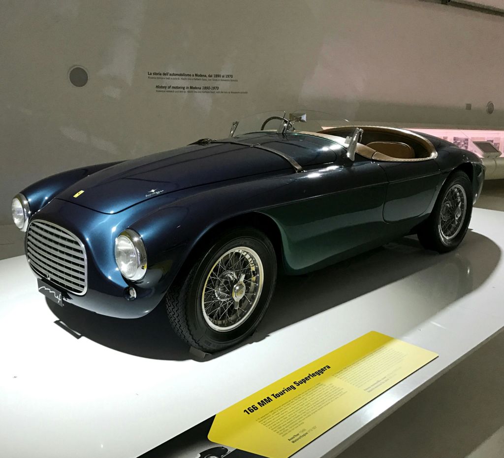 박물관에 노출된 바퀴가 달린 짙은 파란색 빈티지 스포츠카에 노란색 안내패가 함께 전시되어 있습니다.