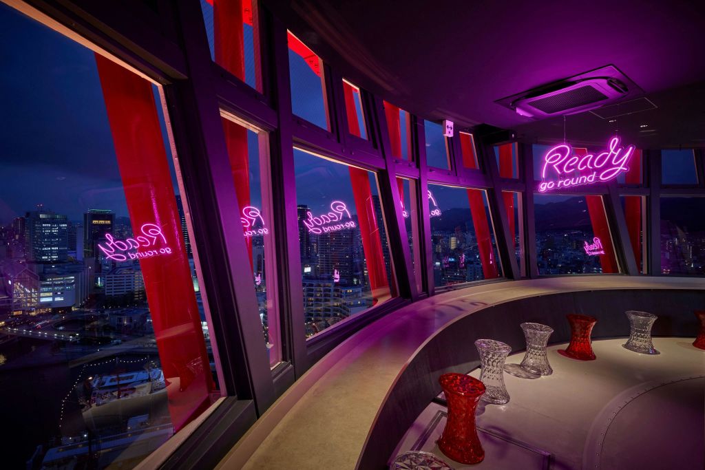 탁자 위에 빨간색과 투명한 유리 제품, 해질 무렵 도시 전망을 감상할 수 있는 커다란 창문이 있는 현대적인 라운지입니다.