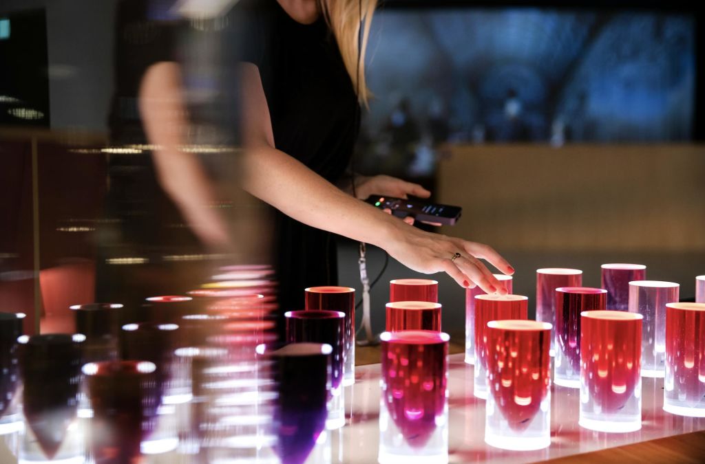 희미하게 빛나는 방에서 빨간색과 분홍색의 다양한 음영의 빛나는 원통형 물체를 만지는 사람.