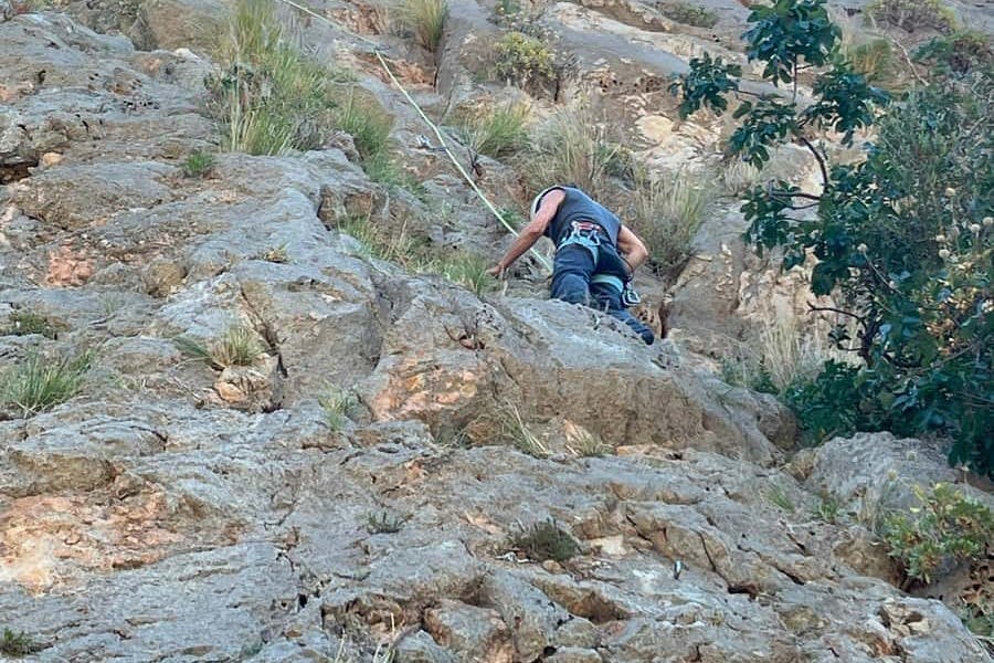 초목으로 바위 절벽을 스케일링하고 바위와 로프를 잡고 지지하는 등반 장비를 착용한 사람.