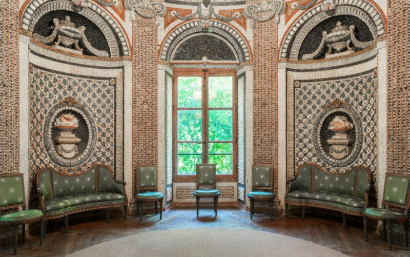 정교한 벽 디자인, 초록색 의자 4개, 외부의 녹음이 우거진 커다란 창문이 있는 화려한 객실입니다.