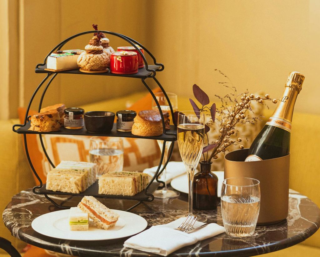 샴페인, 잔, 꽃병과 함께 애프터눈 티를 즐길 수 있도록 테이블에 과자, 스콘, 잼, 샌드위치가 놓인 쟁반입니다.