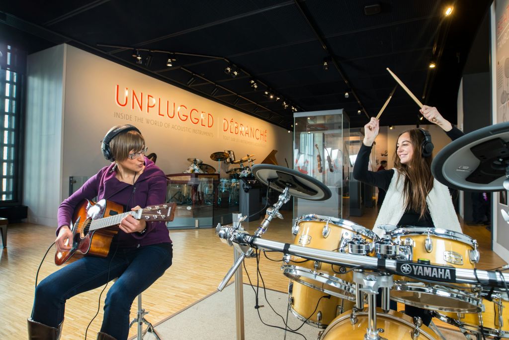 음악 전시회에서 헤드폰을 끼고 기타를 연주하는 사람. 드럼과 "Unplugged" 표시가 배경에 표시됩니다.