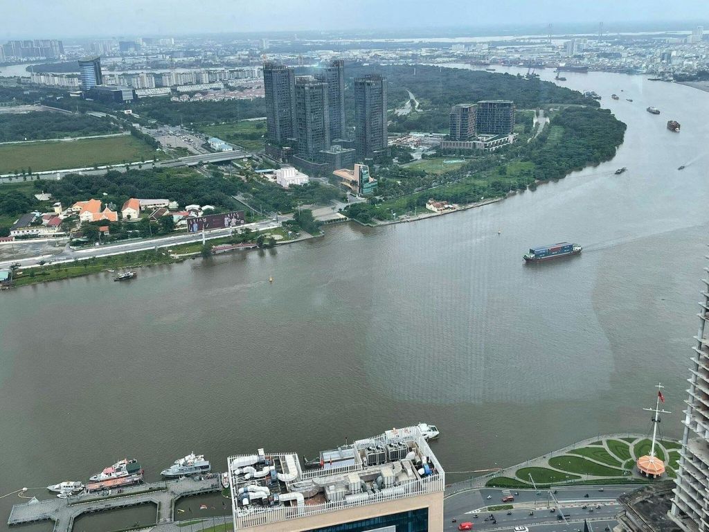 해안가에 보트, 건물, 녹지가 있는 강과 멀리 도시 풍경이 보이는 공중 전망.