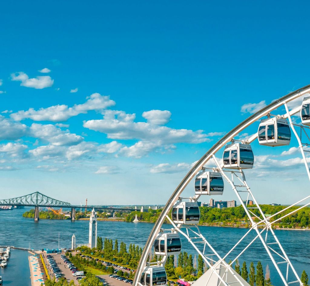 푸르름과 구름이 가득한 밝고 푸른 하늘 아래 스카이라인으로 둘러싸인 다리를 배경으로 강 근처의 대관람차.