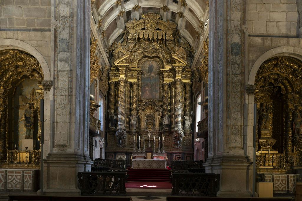정교하게 장식된 교회 제단에는 정교한 조각과 금색 액센트, 그림이 장식되어 있습니다. 돌 기둥과 퓨가 보입니다.