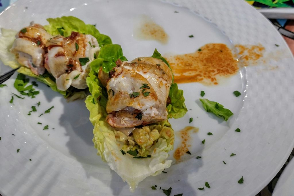 양상추 잎에 닭 조각을 올리고 허브와 소스를 곁들여 흰 접시에 담아 낸다.