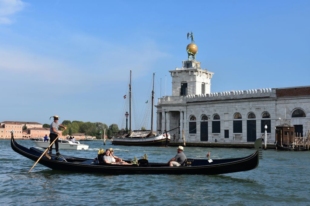 유서 깊은 건물이 있는 운하에서 곤돌라를 타는 사람들과 맑고 푸른 하늘 아래 다른 보트들이 배경을 이루고 있습니다.