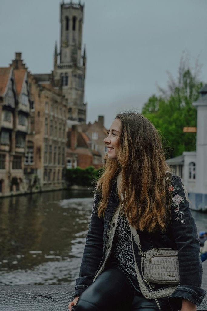 유서 깊은 건물과 시계탑을 배경으로 운하 옆에 긴 머리카락을 한 여성이 서 있습니다.