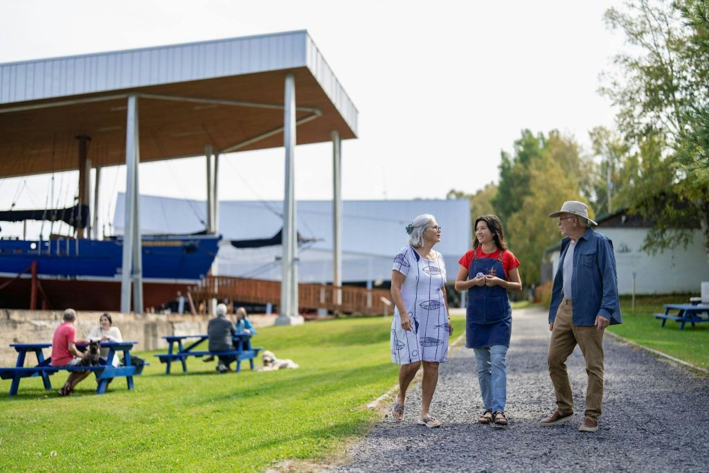 건물과 피크닉 테이블을 배경으로 공원 같은 공간에서 자갈길을 걷는 세 사람.