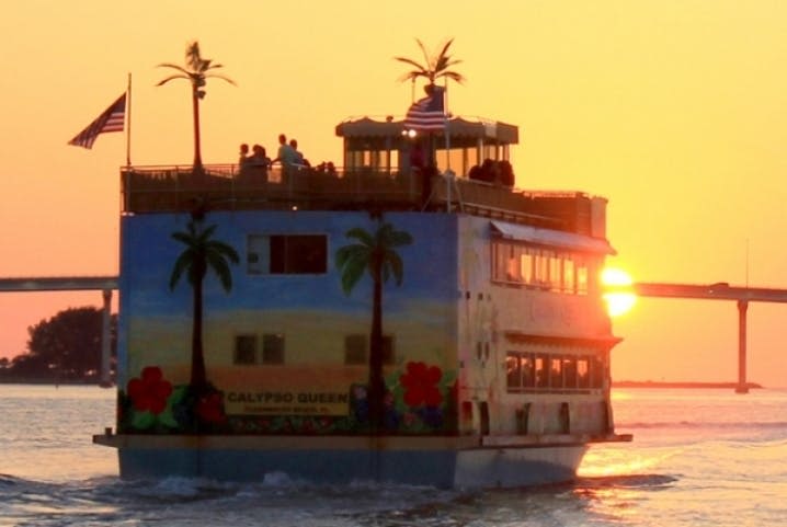 "칼립소 퀸" 이라는 이름의 페리로, 일몰에 열대 벽화가 그려진 항해가 펼쳐집니다. 탑승객은 상부 갑판에 있습니다.