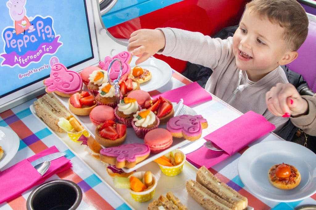 생동감 넘치는 배경과 함께 컵케이크, 마카롱, 샌드위치 등 다채로운 과자 테이블을 즐기는 아이.