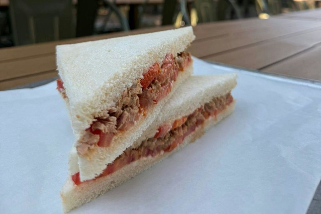 흰 빵, 참치, 토마토 조각이 들어간 샌드위치를 클로즈업하여 양피지 종이 위에 나무 테이블 위에 올려놓습니다.