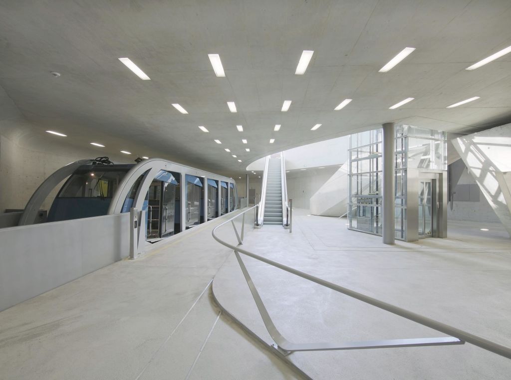 세련된 모노레일, 에스컬레이터, 유리로 둘러싸인 엘리베이터가 있는 현대적인 실내 기차역. 천장 설비의 밝은 조명.