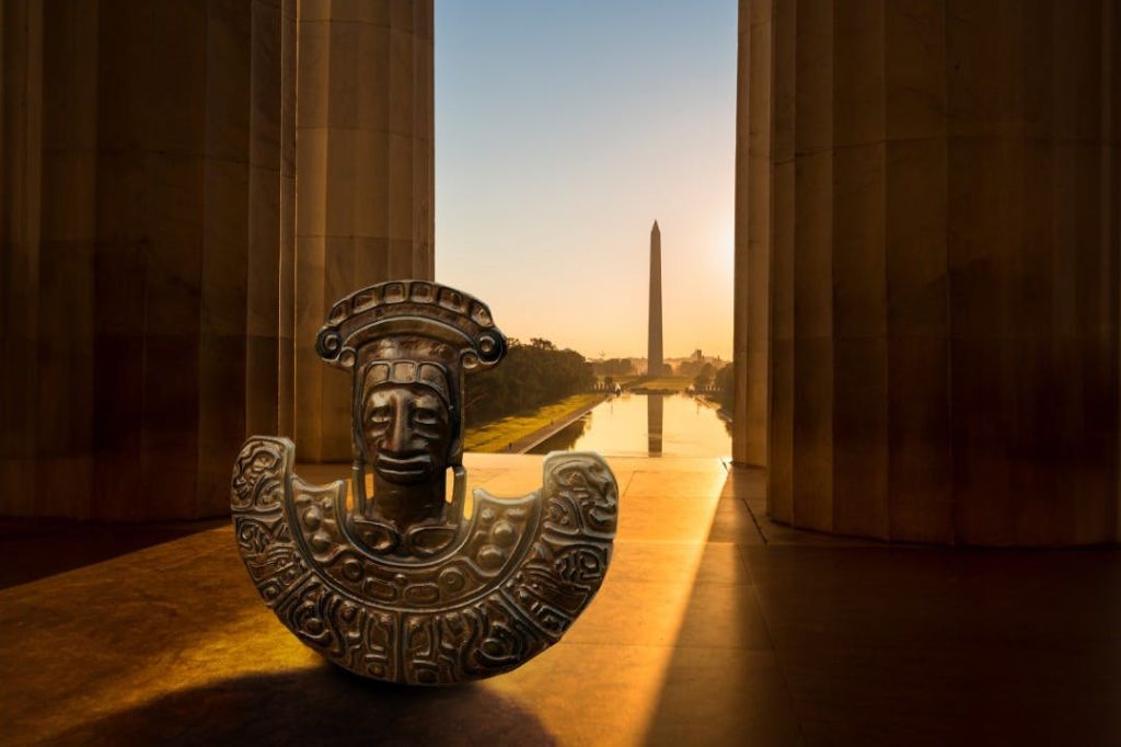 기둥 사이로 석양이 질 무렵, 워싱턴 기념비와 리플렉팅 풀이 한눈에 내려다보이는 전경의 고대 조각상.