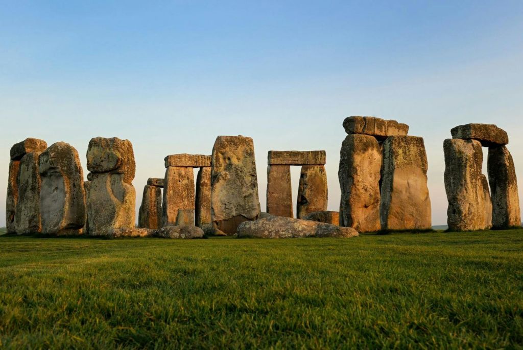 석양이 지는 맑고 푸른 하늘 아래 잔디밭에 서 있는 고대 석원 기념비인 스톤헨지 (Stonehenge).