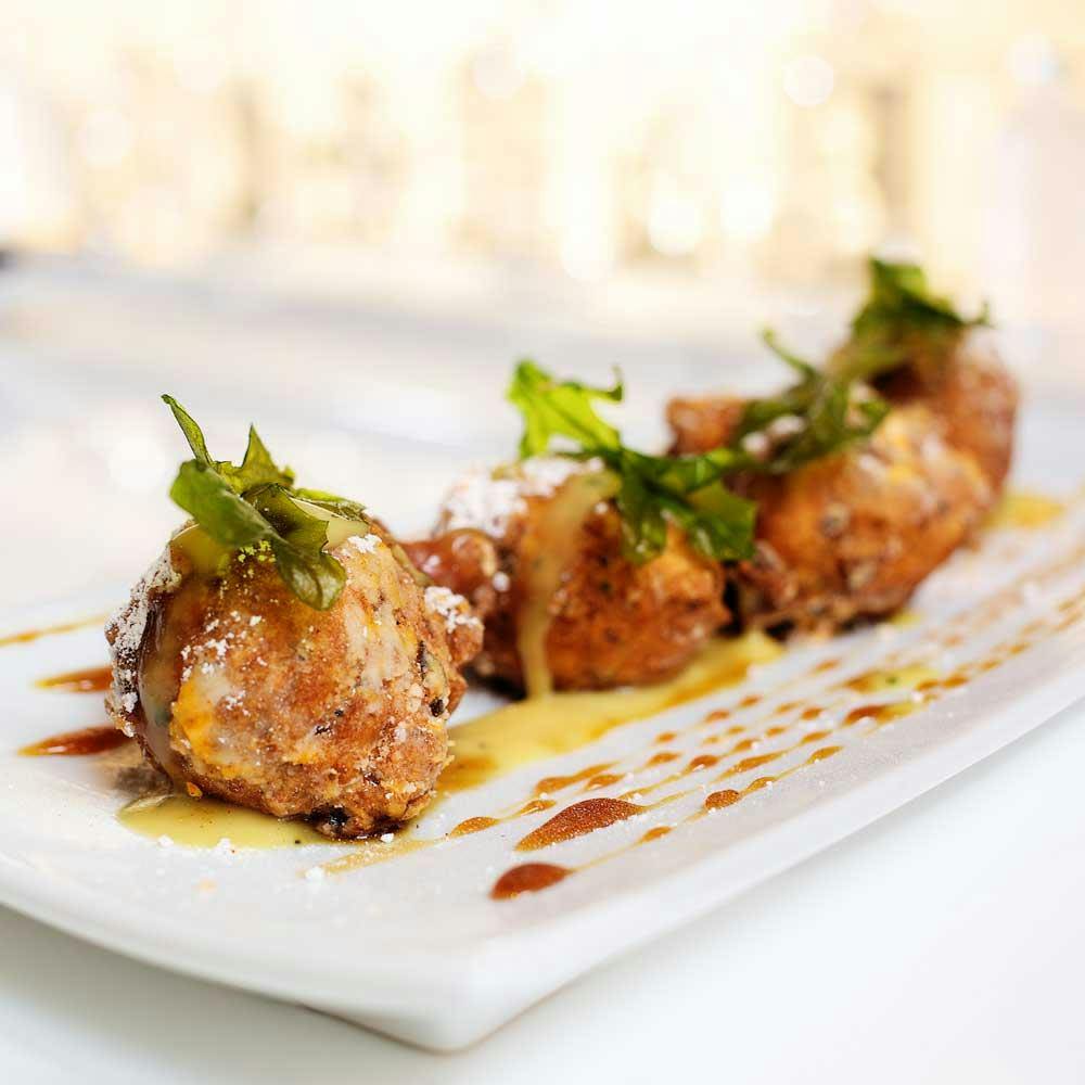 하얀 직사각형 접시에 허브를 장식하고 소스를 뿌린 후 가루를 뿌린 튀긴 음식이 담긴 접시.