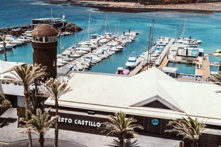 수많은 도킹 보트, 청록색 물, 원통형 석탑, "푸에르토 카스티요" 라고 적힌 건물이 있는 마리나. 전경의 야자수.