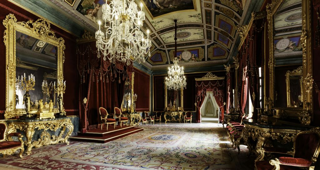 화려한 샹들리에, 붉은 드레이프, 금박 의자, 디테일한 천장 페인팅이 있는 호화로운 객실로, 왕좌의 방을 제안합니다.