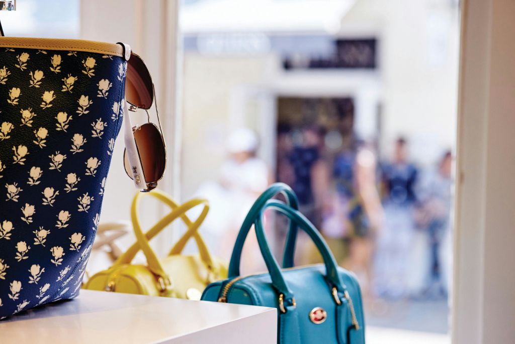 매장에는 핸드백과 선글라스가 진열되어 있으며, 흐릿한 사람들이 바깥을 배경으로 걸어다니고 있습니다.