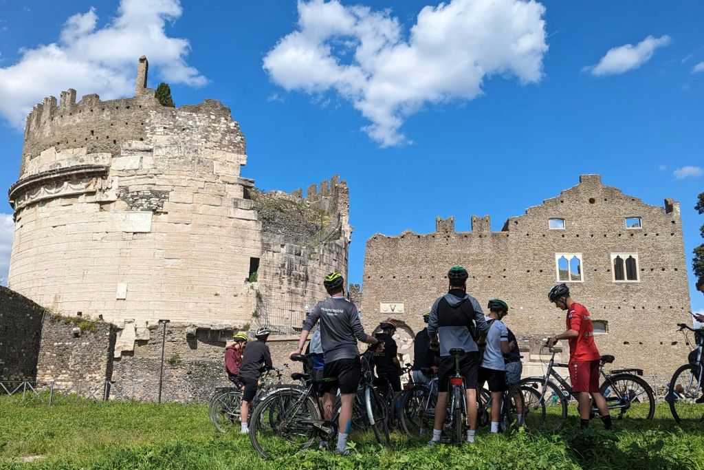푸른 하늘과 구름이 있는 화창한 날, 고대 유적지 근처에서 자전거를 타고 서 있는 한 무리의 자전거 타는 사람들.