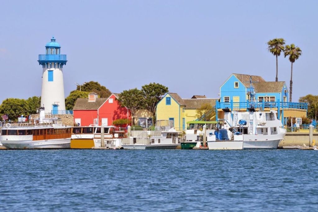 수변에는 화려한 건물과 보트가 줄지어 있으며, 왼쪽에는 등대가, 위에는 맑고 푸른 하늘이 있습니다.