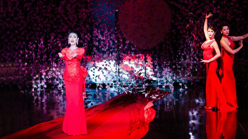 빨간색 드레스를 입은 두 명의 여성이 무대에서 꽃잎을 배경으로 빛나는 바닥을 배경으로 공연을 펼칩니다.