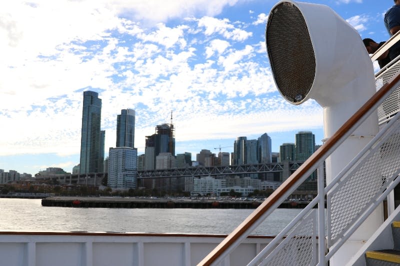 난간과 대형 스피커가 있는 보트 갑판에서 보이는 높은 건물과 다리가 있는 도시 스카이라인의 전망.