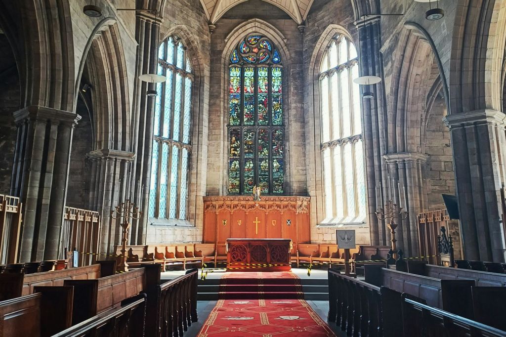 석조 아치와 스테인드글라스 창문이 있는 교회 내부와 목조 페우가 있는 제단으로 이어지는 레드 카펫.
