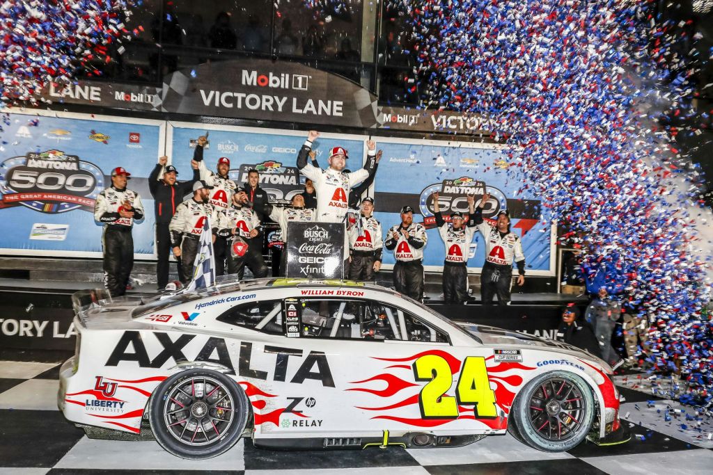 경주용 자동차 운전자가 "AXALTA" 라고 표시된 경주용 자동차와 색종이로 둘러싸인 숫자 "24" 뒤에 있는 팀과 함께 연단에서 축하합니다.