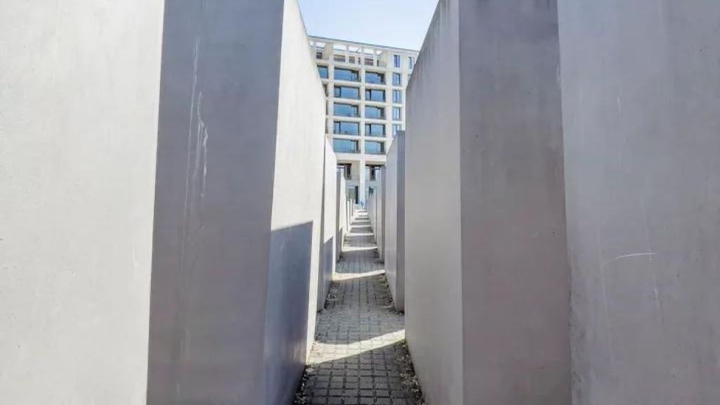 높은 콘크리트 블록으로 둘러싸인 좁은 통로는 배경의 현대적인 유리 건물로 이어집니다.