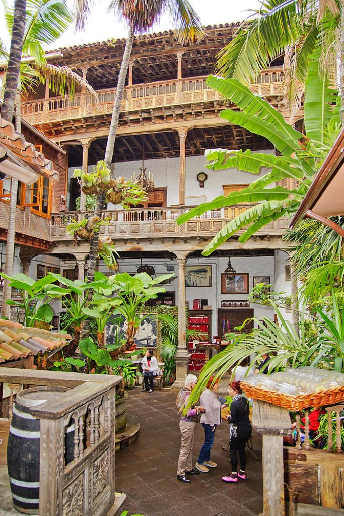 식물로 둘러싸인 사람들로 둘러싸인 울창한 마당과 섬세한 건축물이 특징인 다층 목조 발코니.